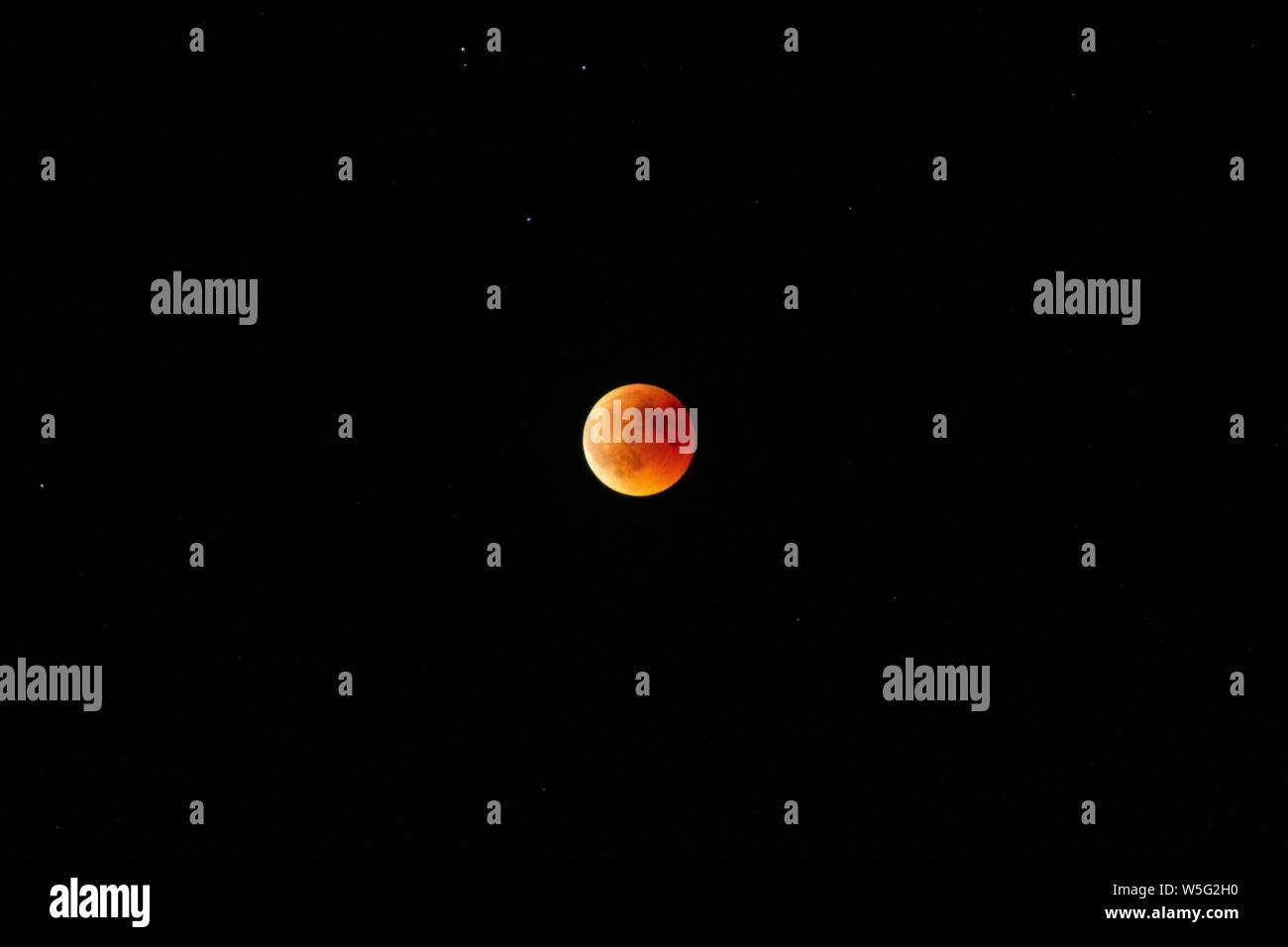 Horizontal long shot of an orange and red moon in the dark sky at night Stock Photo