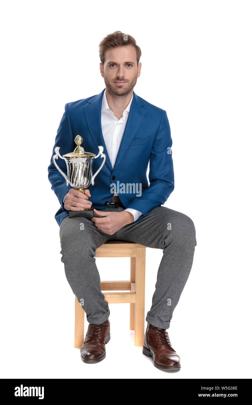 Young casual man holding his trophy on his lap while wearing a suit and ...