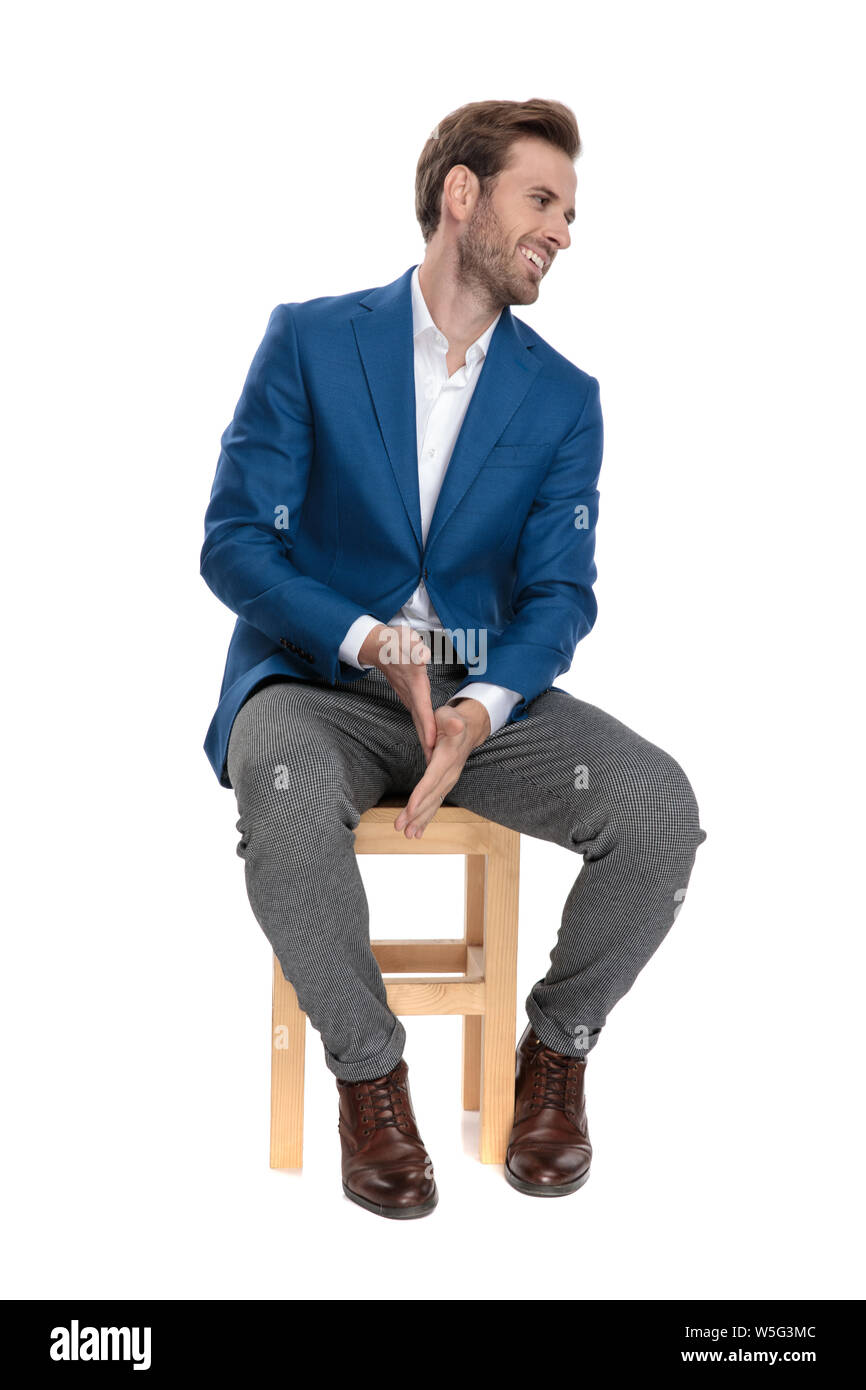 Merry casual guy laughing and rubbing his hands while sitting on a chair  and wearing a suit on white studio background Stock Photo - Alamy