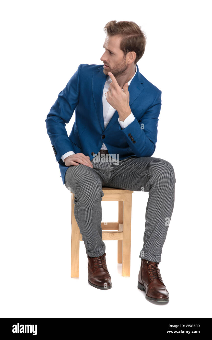 Powerful businessman ordering and pointing while confidently looking to the side, wearing a suit and sitting on a chair, on white studio background Stock Photo