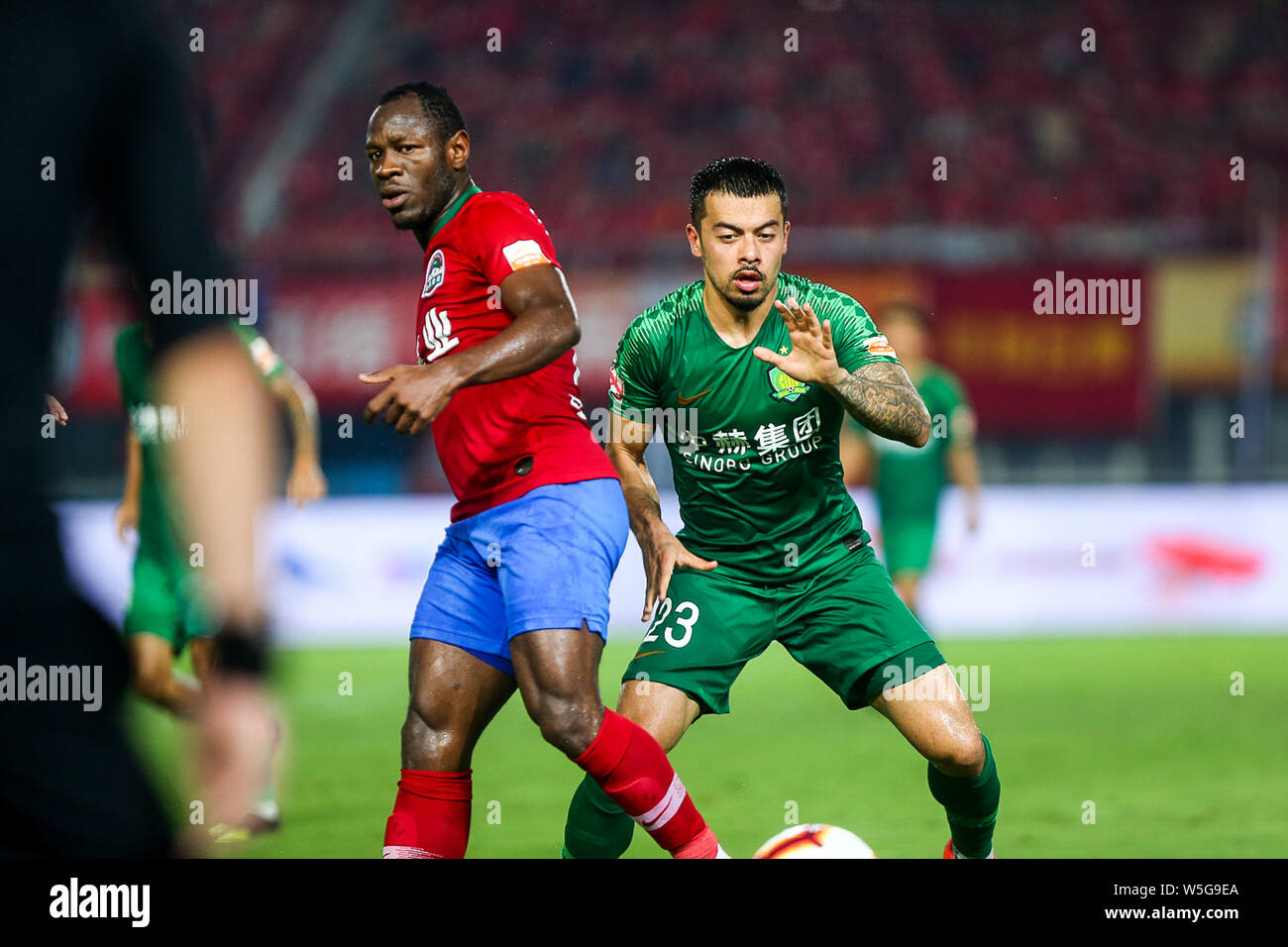 Cameroonian football player Christian Bassogog, left, of Henan Jianye passes the ball against English football player Nico Yennaris, known in China as Li Ke, of Beijing Sinobo Guoan in their 20th round match during the 2019 Chinese Football Association Super League (CSL) in Zhengzhou city, central China's Henan province, 27 July 2019. Henan Jianye defeated Beijing Sinobo Guoan 1-0. Stock Photo