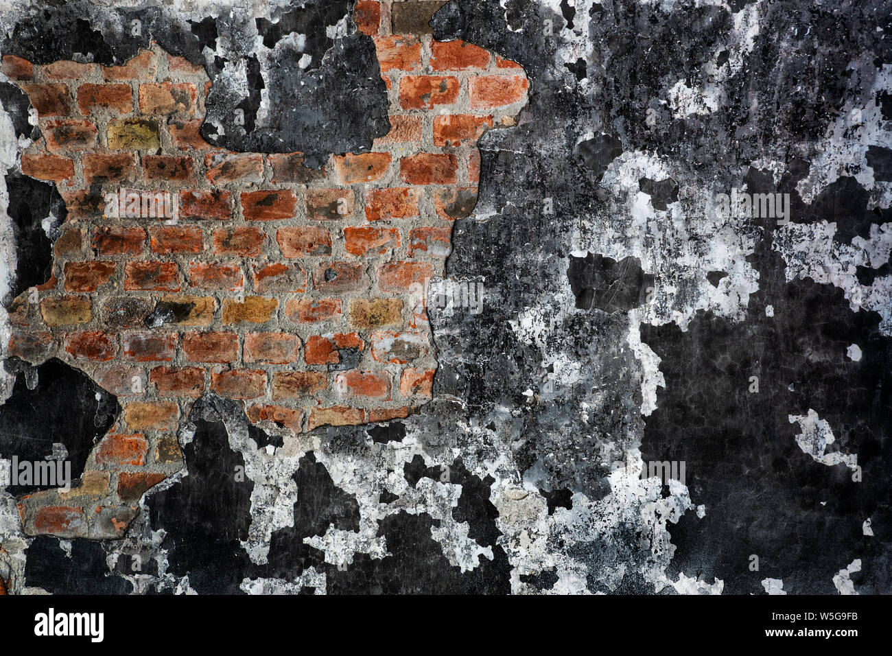 Wall with a burnt peeling paint, now black used to be white, revealing brick structure under plaster in an old, abandoned building, grunge background Stock Photo