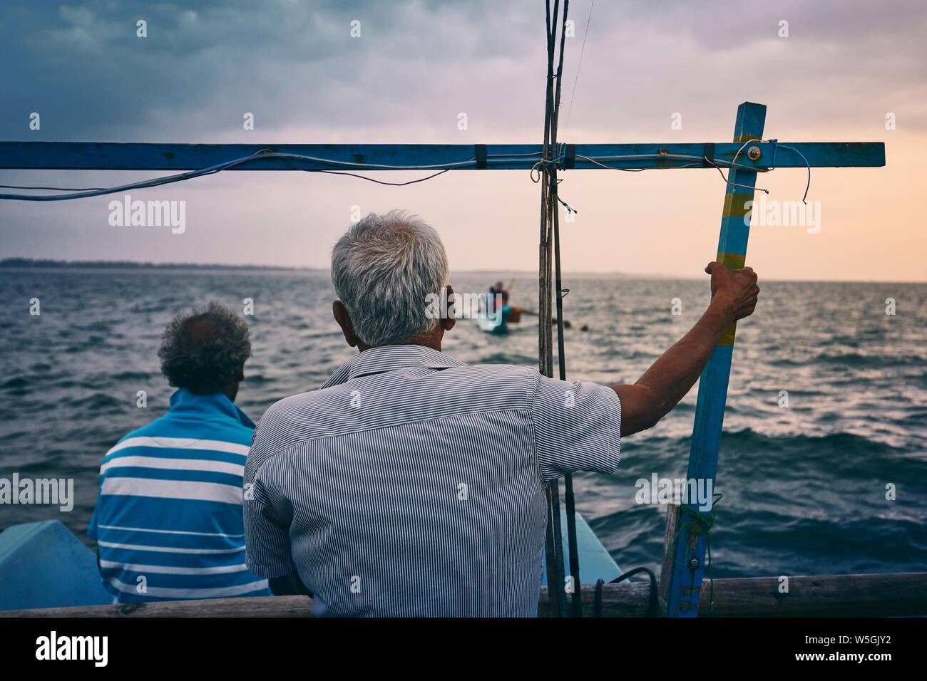 Hard work on sea. Two fishermen on fishing boat at sunrise near coastline of Sri Lanka. Stock Photo