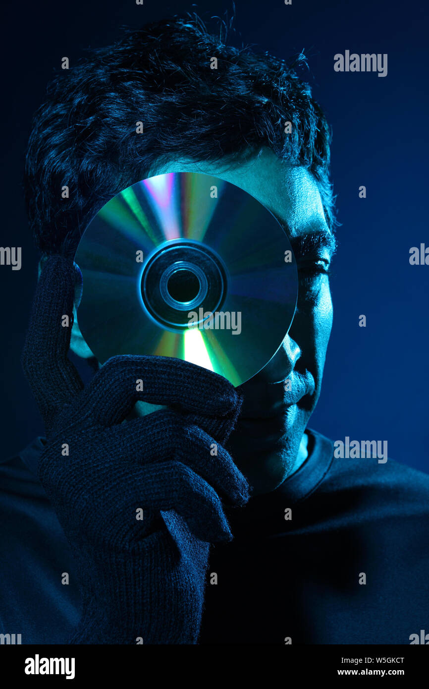Hacker holding a pirated compact disc in front of face Stock Photo