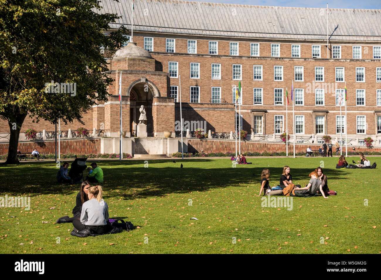 Young people sitting on grass at College Green having conversation, Bristol, UK Stock Photo
