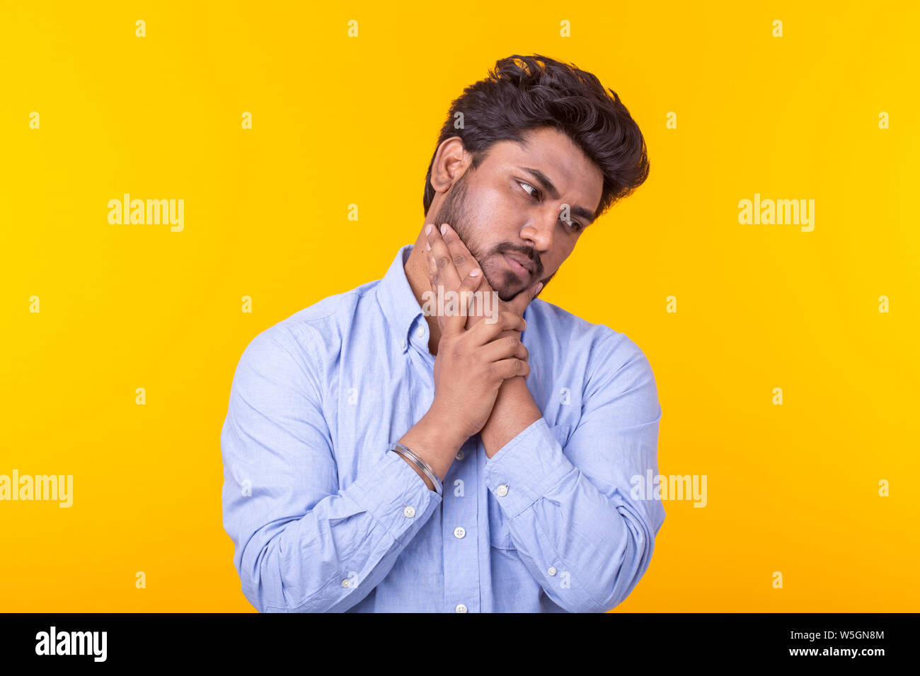 Apathetic cute young indian man is posing on a yellow background with copy space and thinking about something. Concept of unfulfilled dreams. Stock Photo