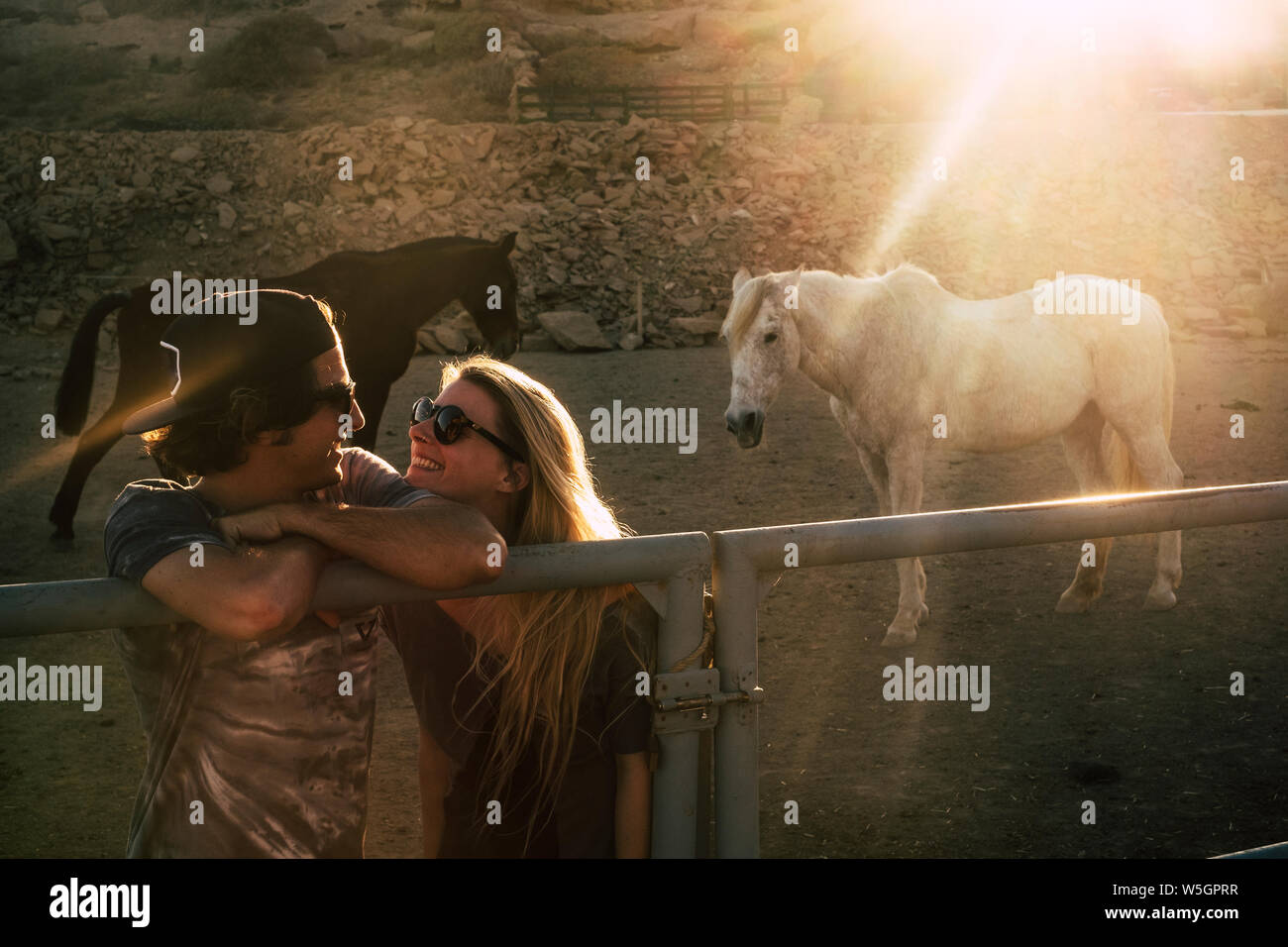 Young cheerful people happy couple outdoor in romantic relationship with horses and sunset in background - concept of alternative lifestyle for millen Stock Photo