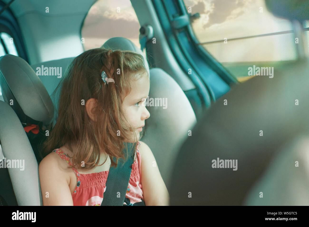 Caucasian blonde little girl sitting on a infant car sear in a car journey looking throw the window. Security concept with empty copy space for Editor Stock Photo