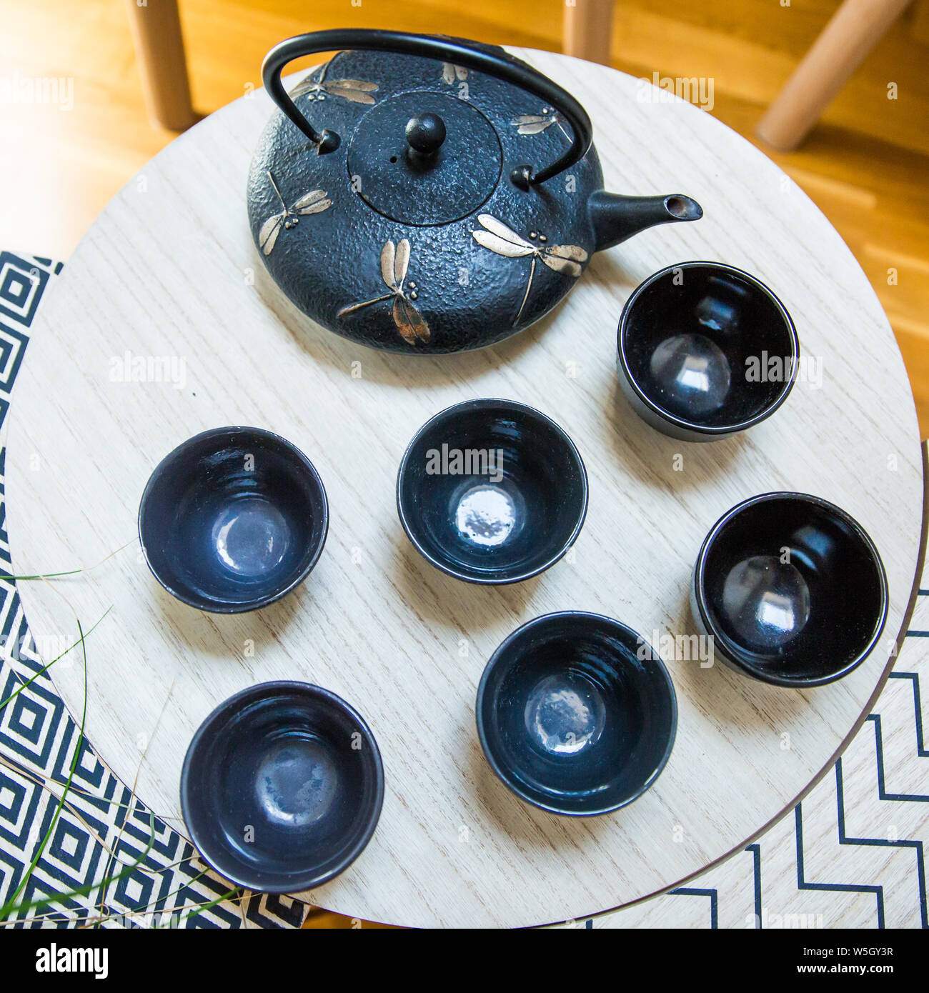 Stylish Interior Decoration of a Cast Iron Teapot with Dragonfly Decoration and Round Cups on Geometric Tables Stock Photo