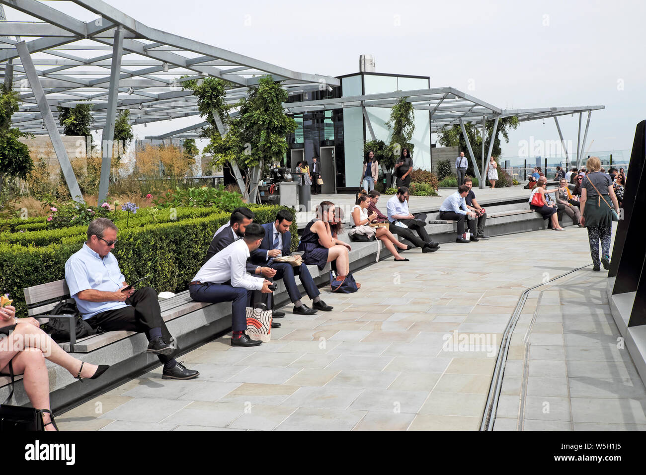 People At Lunchtime Sitting On Benches Eating Lunch On Terrace At