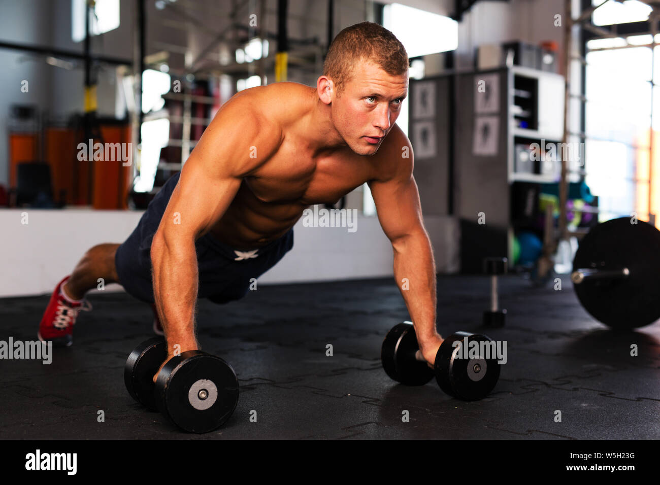 Young man doing pushups on dumbbells at gym Stock Photo