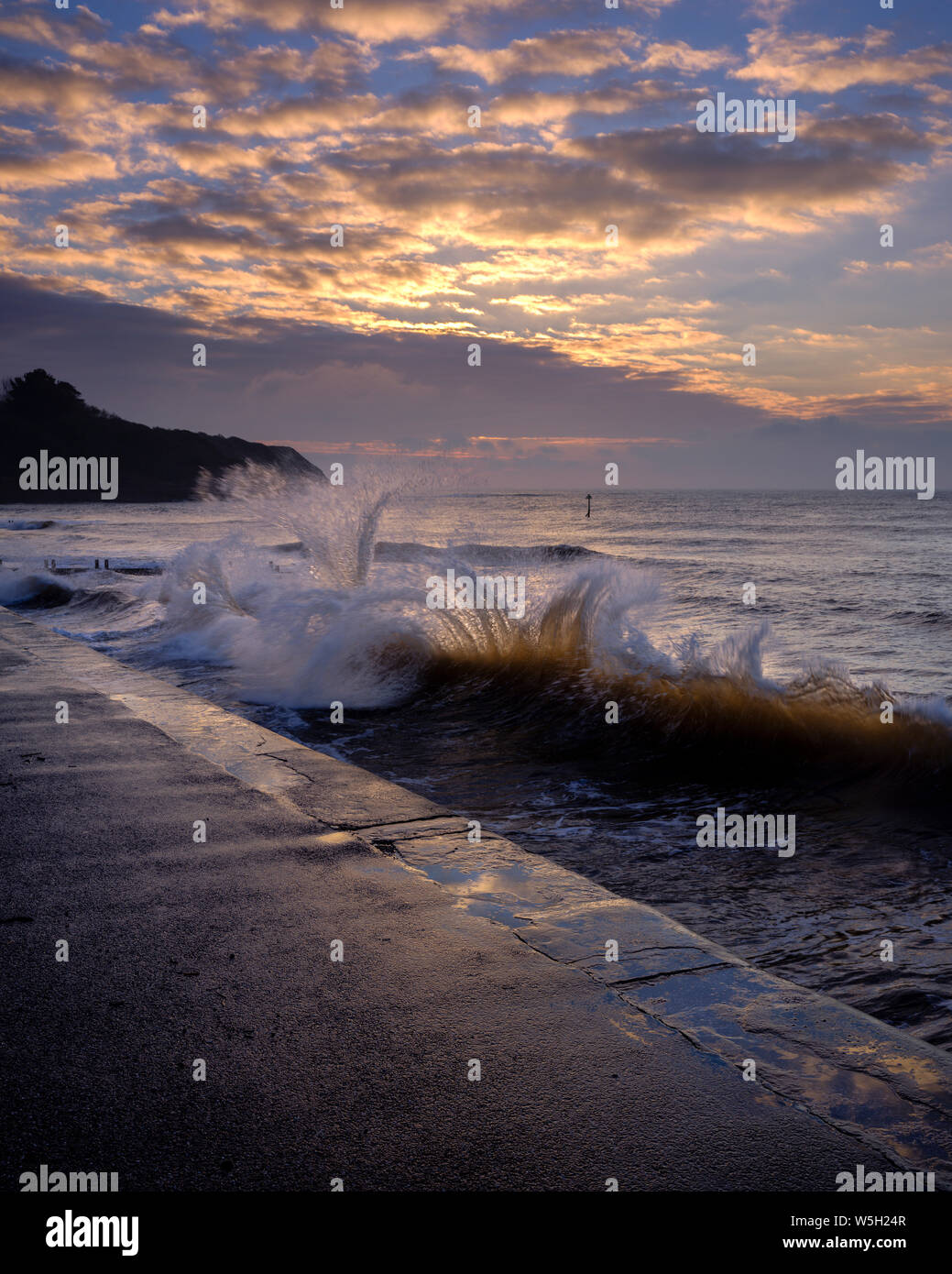 Waves backlit by the dawn sun reflect off the sea wall and impact with an incoming one, Exmouth, Devon, England, United Kingdom, Europe Stock Photo