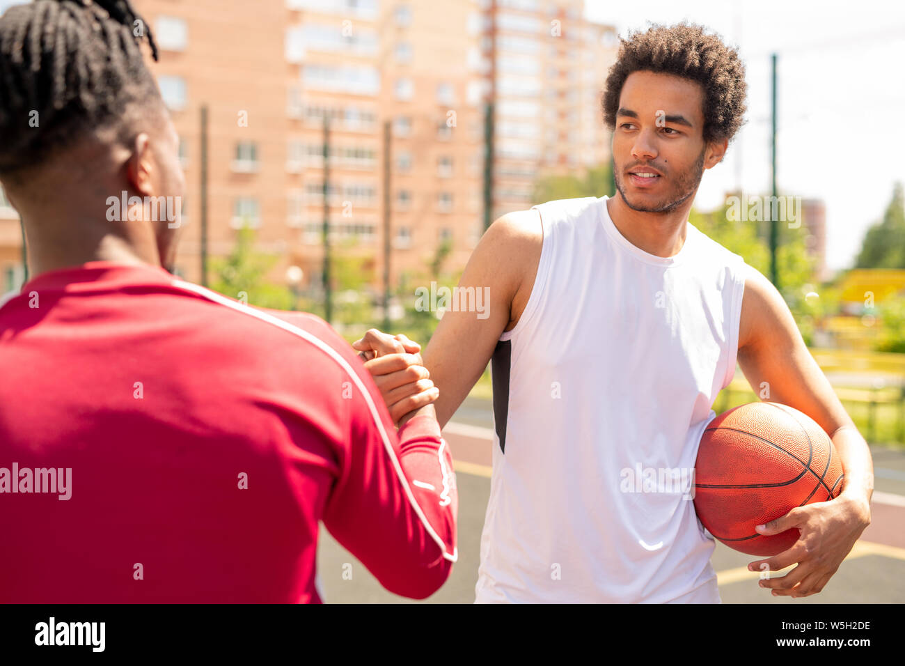 Young intercultural sportsman with ball shaking hand of his playmate Stock Photo