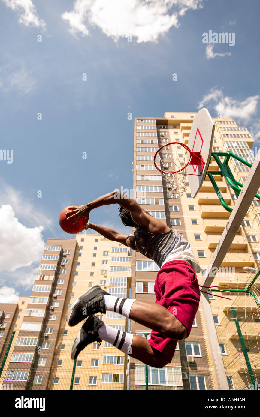 View from below of young African basketballer in jump throwing ball in
