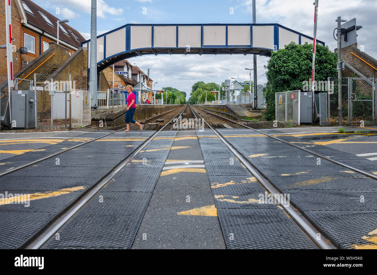 A view along tracks passing under a footbridge and through Datchet railway station taken from a level crossing. Stock Photo