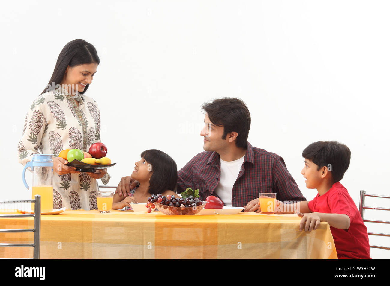 Woman serving fruits in breakfast to her family Stock Photo