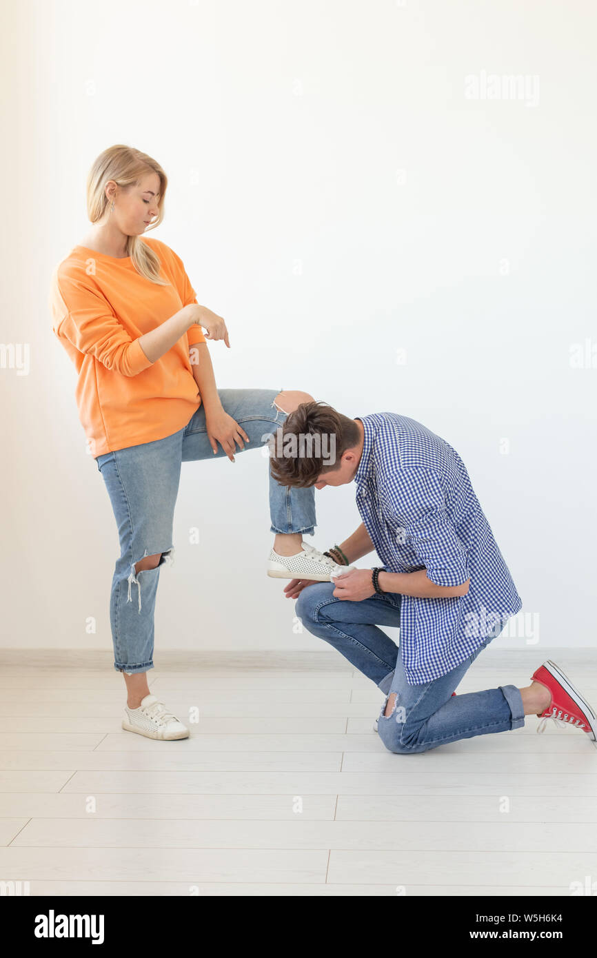Young man tying shoelaces of his beloved woman posing on the white background. Concept of courtship and reverent relationships. Stock Photo