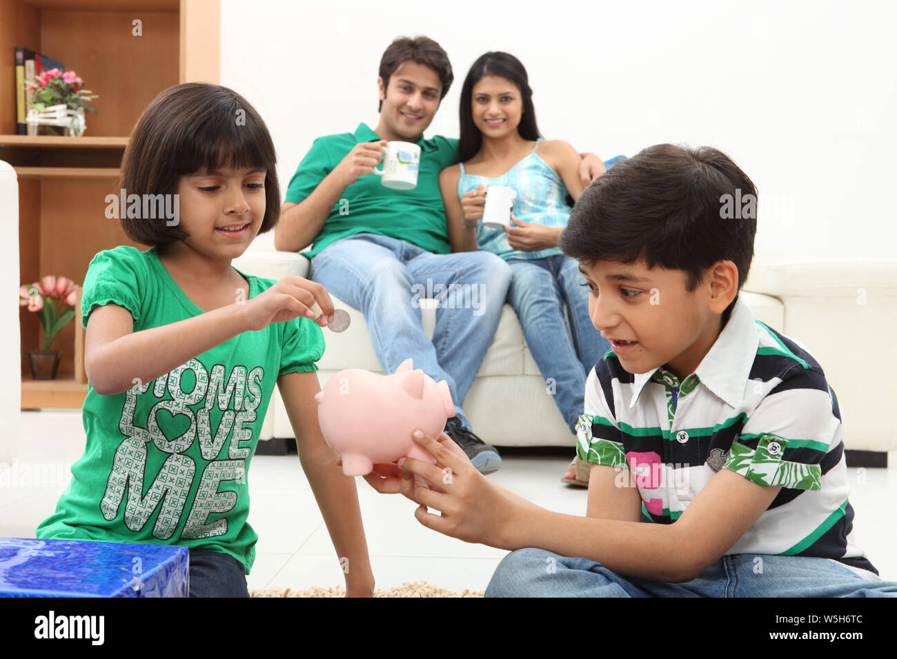 Girl putting coin into a piggy bank with her brother Stock Photo - Alamy