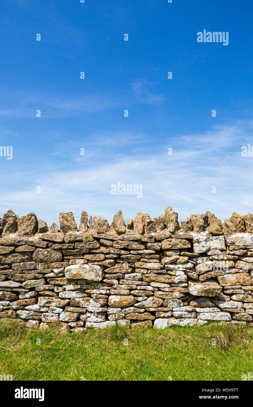 A Cotswold stone wall against a blue sky with Cirrus clouds Stock Photo