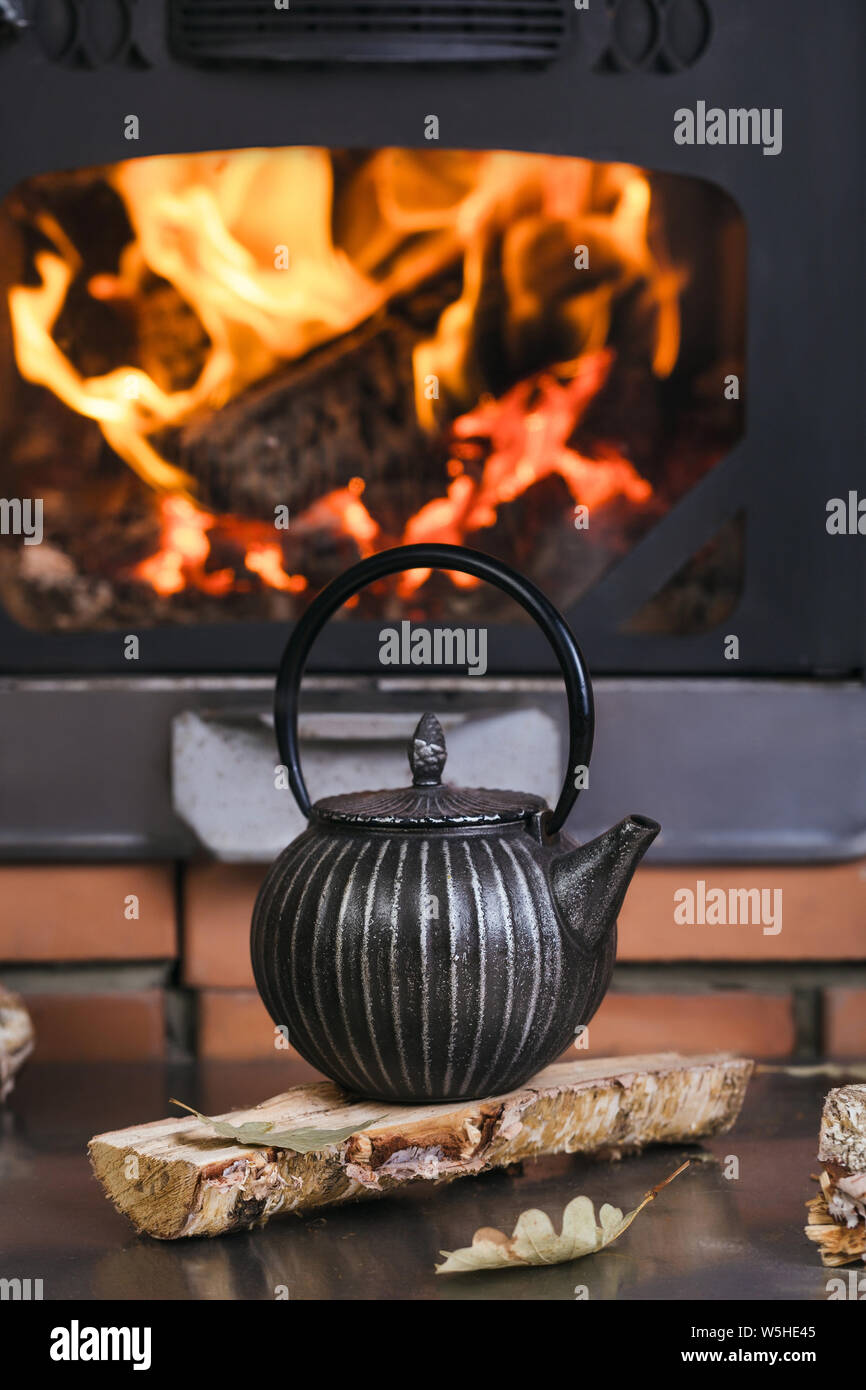 Comfort interior with closed burning fireplace. Composition cast iron kettle firewood Stock Photo Alamy