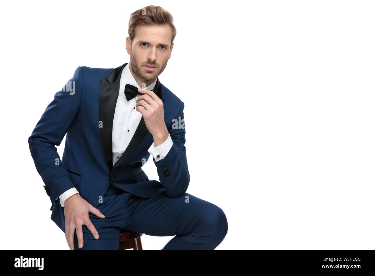 fashion man in blue suit adjusting his bowtie while sitting with hand ...