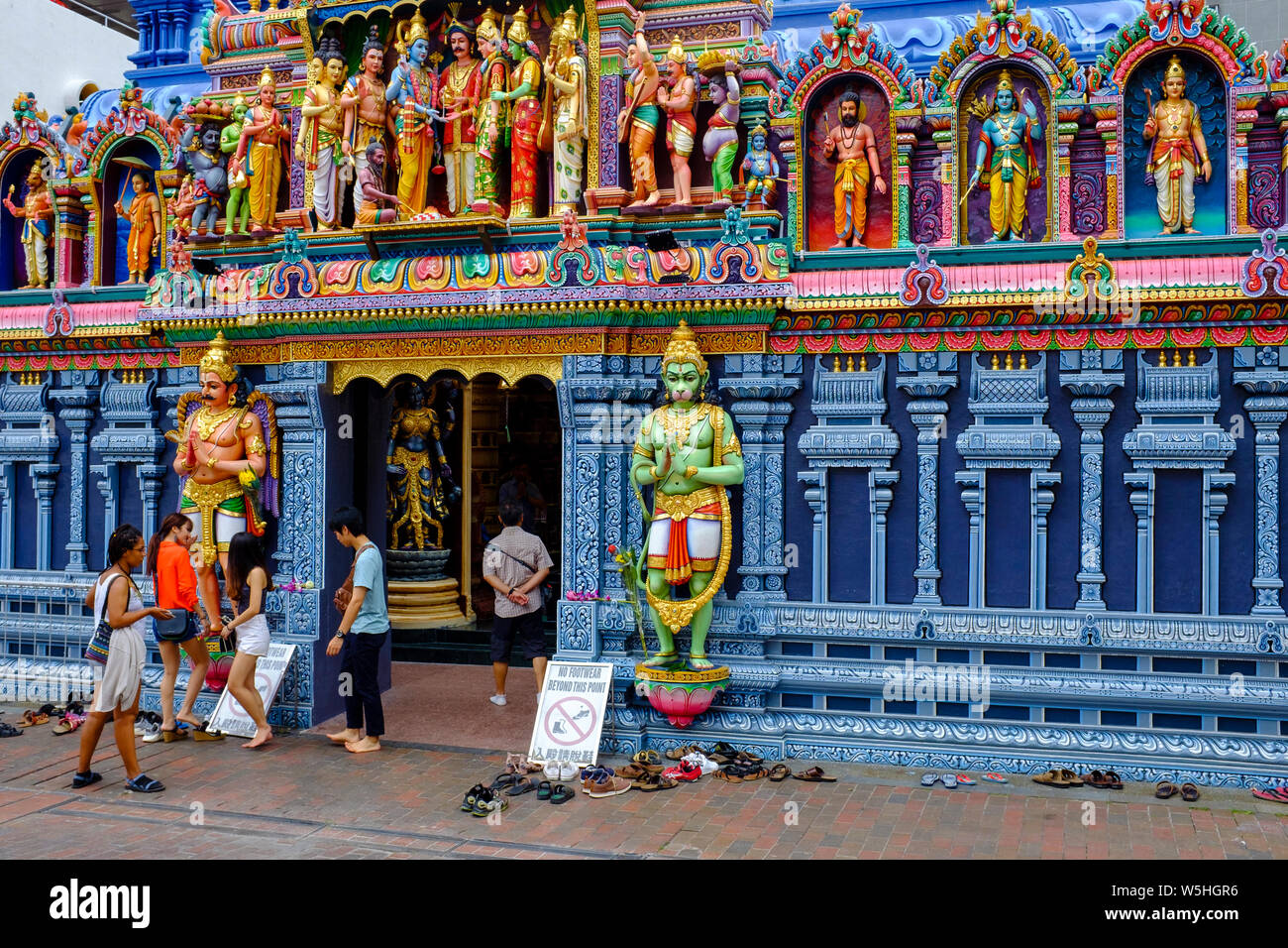 People and shoes outside Sri Krishnan Temple, a hindu temple in Waterloo St Singapore. Signs at the front instruct visitors to remove their footwear. Stock Photo