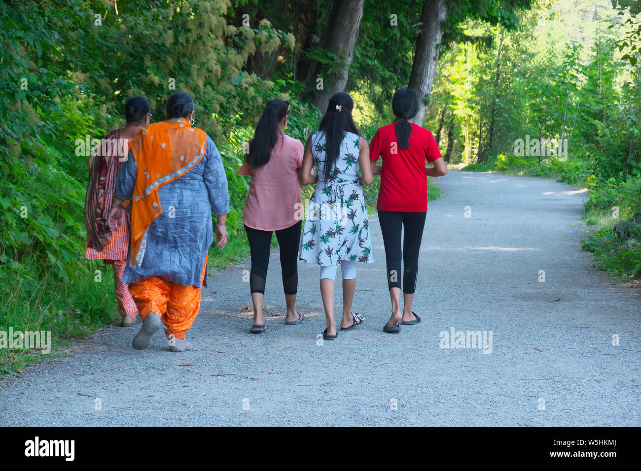 Five Middle Eastern woman in colourful clothing walking along a tree-lined pathway towards the hot mineral waters of Harrison Hot Springs. Stock Photo