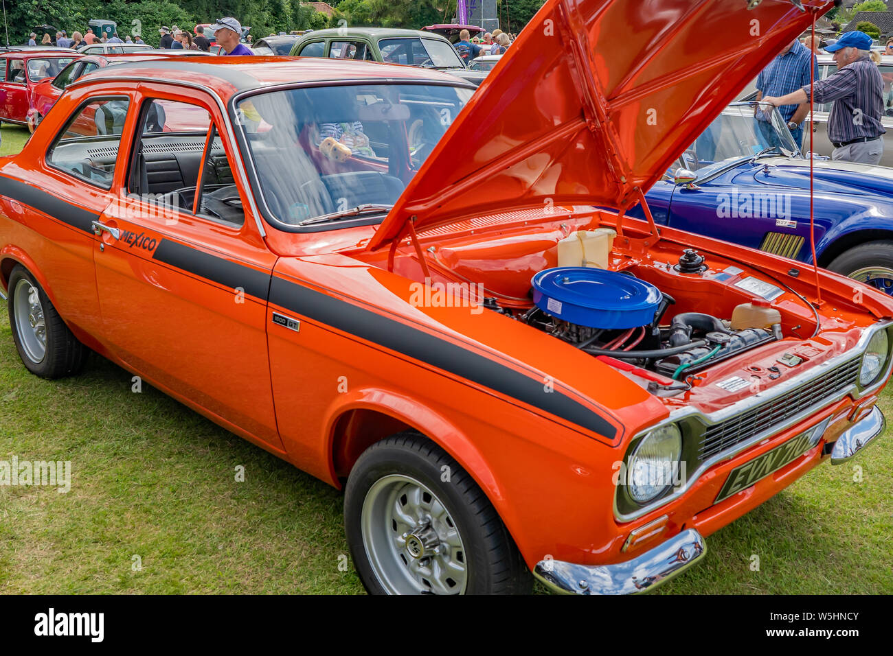 Side view of an orange Ford Mexico replica rally car with a raised