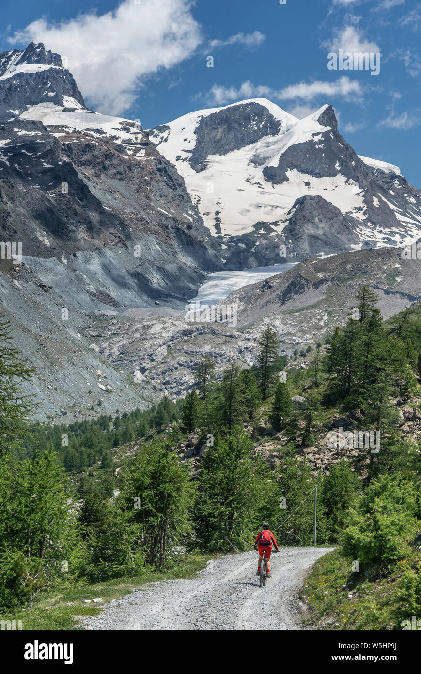 active senior woman, riding her electric mountainbike below the famous Gornergrat in Zermatt, in the background Rimpfischhorn and Strahlhorn,Wallis,Sw Stock Photo