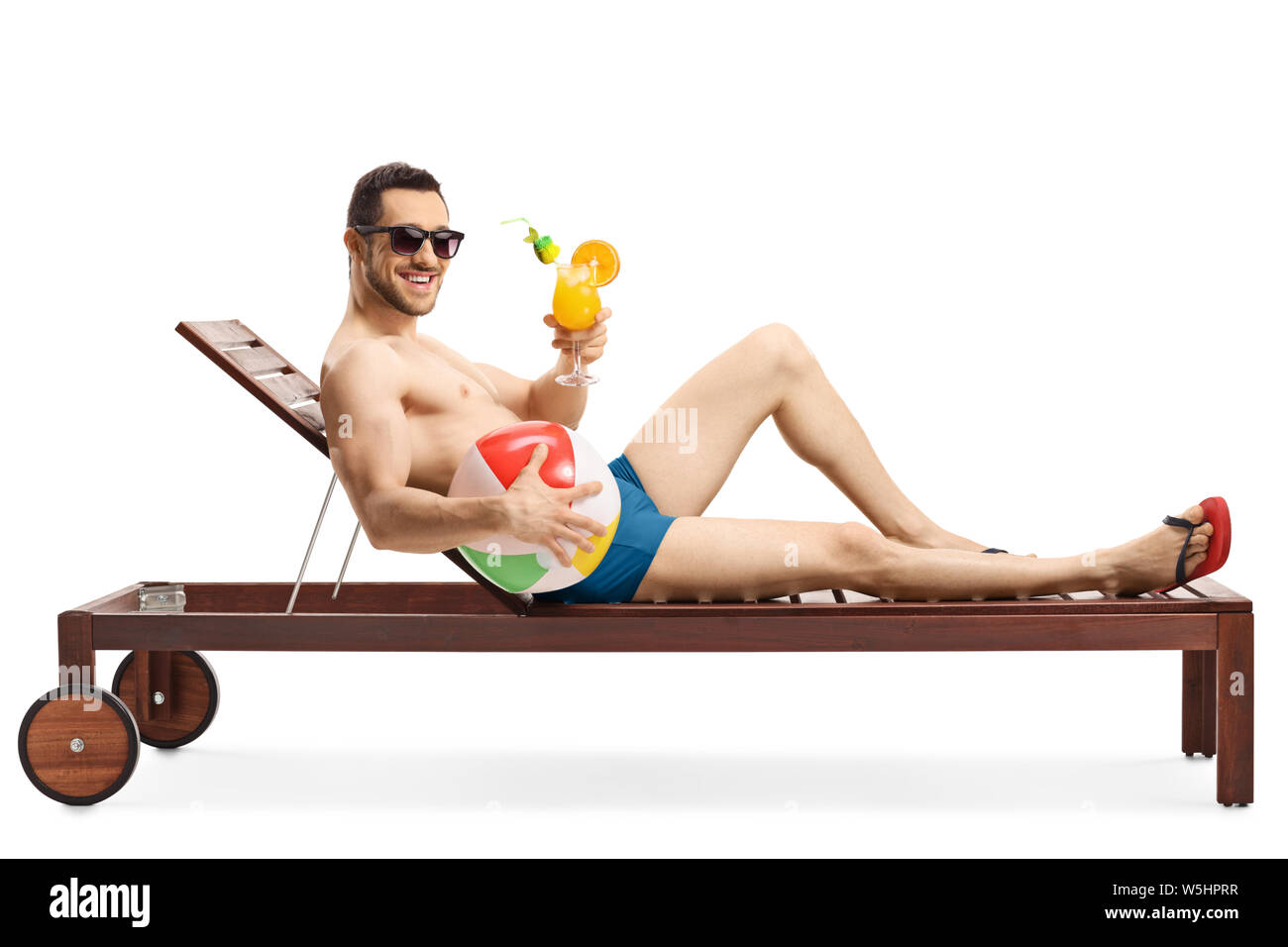 Full length shot of a guy on a lounge bed holding an inflatable ball and a cocktail isolated on white background Stock Photo