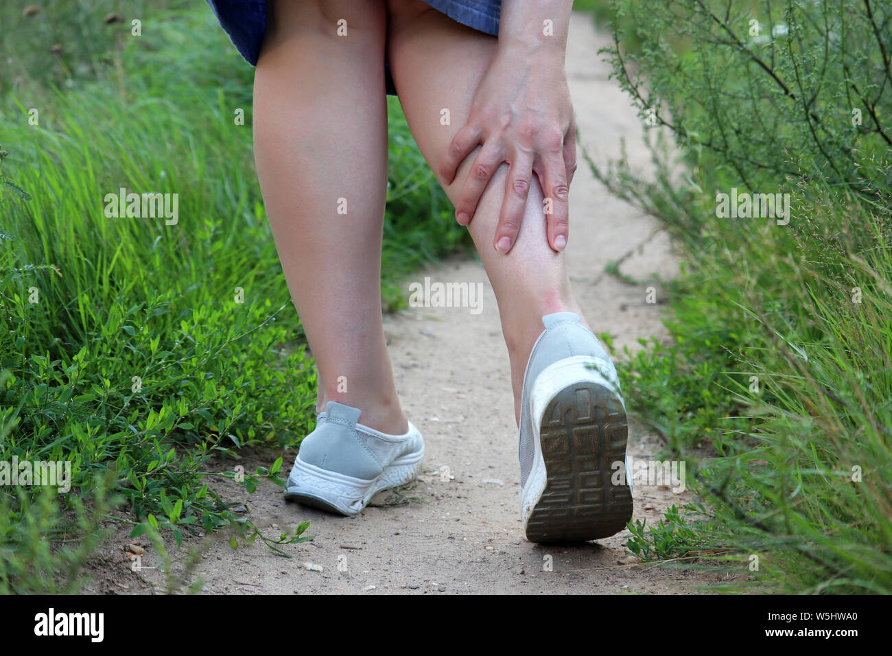 Ankle sprain, woman grabbed her leg while walking on a summer nature. Concept of pain in tired legs, injury on running Stock Photo