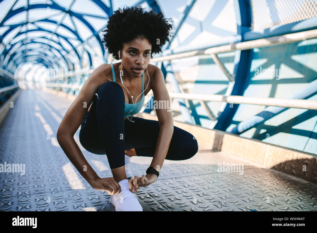 Focused african woman in fitness wear tying her shoelace. Fitness woman