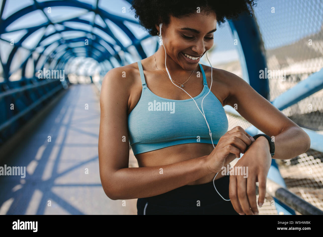 Fit female runner using smart watch to monitor her performance. African Woman setting fitness app on her smart watch before running session. Stock Photo