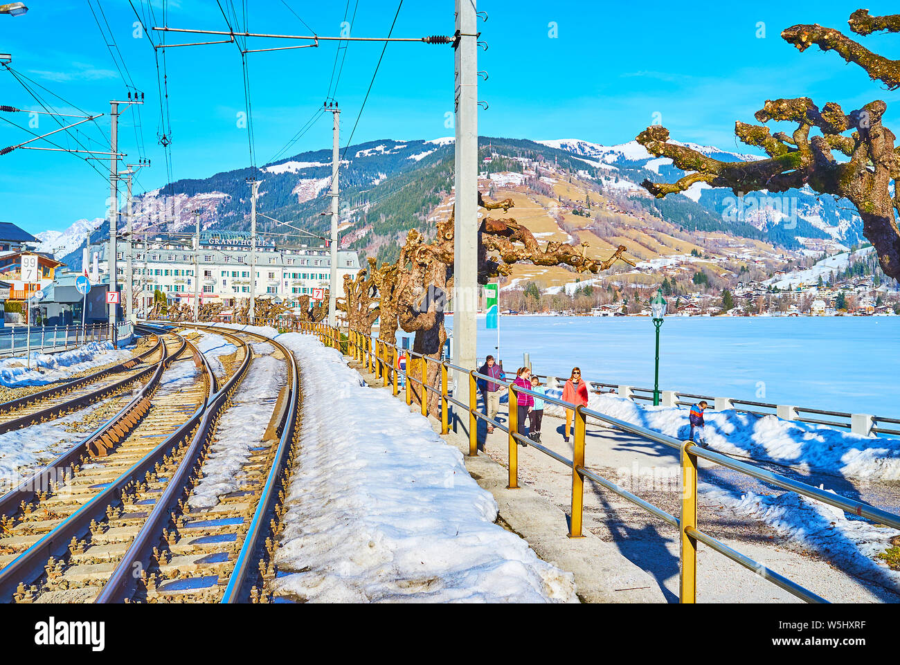 ZELL AM SEE, AUSTRIA - FEBRUARY 28, 2019: The cityscape with railroad, winter Elisabeth park, frozen Zeller See lake and luxury Grand Hotel on backgro Stock Photo
