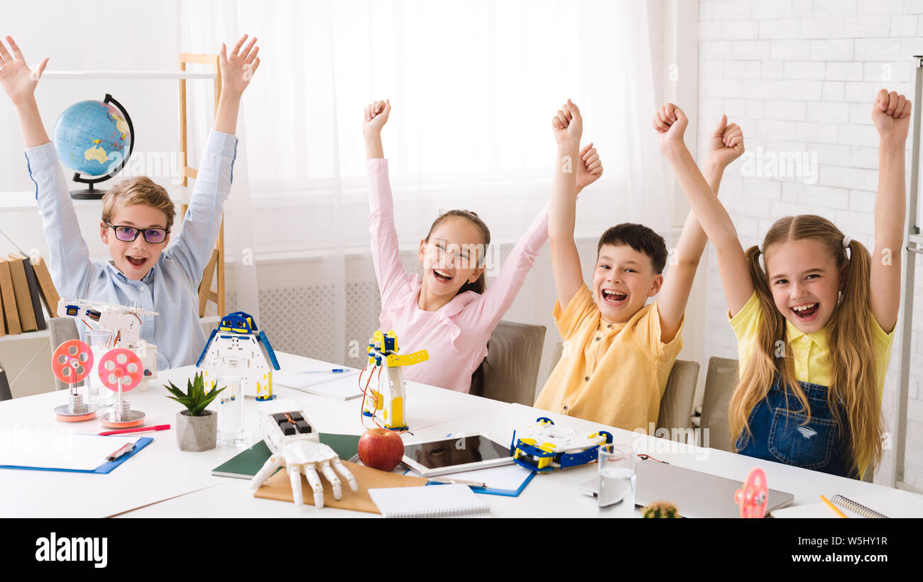 Happy children with raised hands after robotics class Stock Photo