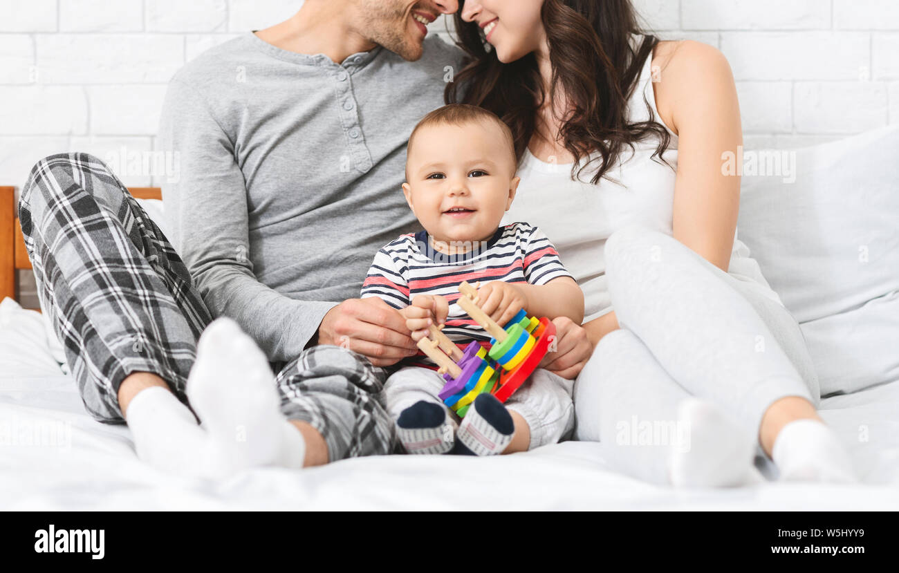 Sweet little baby smiling, sitting on bed with loving parents Stock Photo