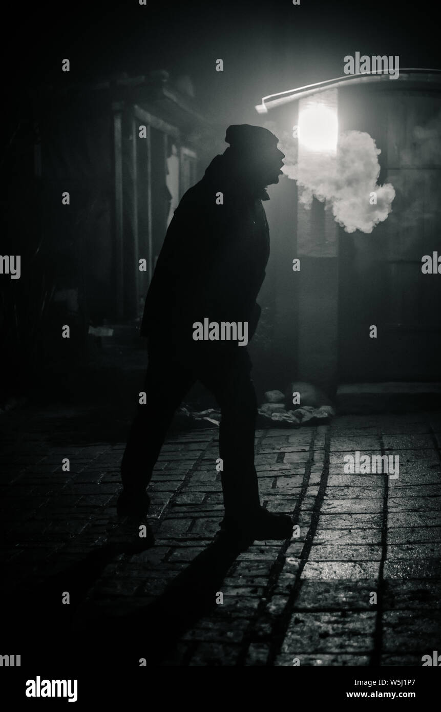 man silhouette smoking like chimney at night with backlight Stock Photo