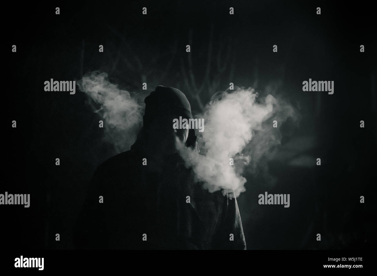 man silhouette smoking like chimney at night with backlight Stock Photo