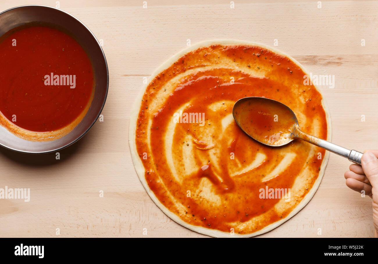 Chef spreading tomato sauce on pizza base Stock Photo