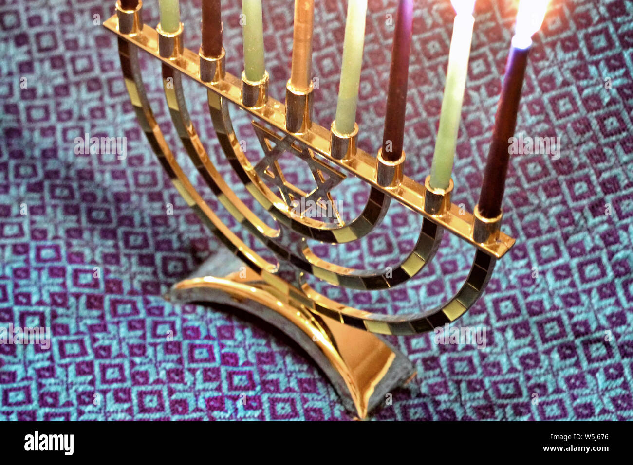 A Star of David themed hanukkiah or Hanukkah candle holder sits atop a blue patterned cloth. Stock Photo