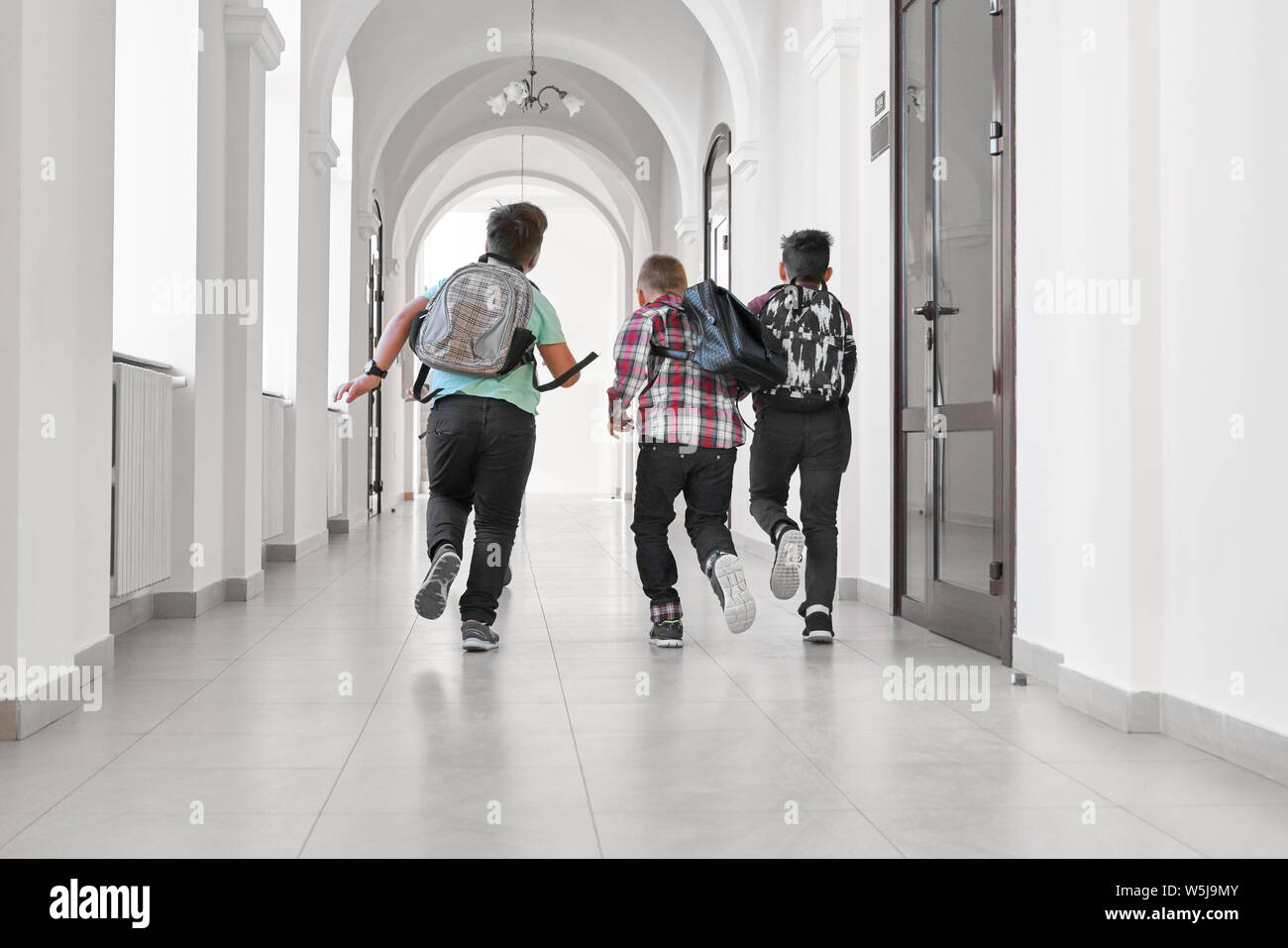 Group of schoolboys with school backpacks running in hallway of school. Classmates having fun and running in break between lessons or after lessons. Stock Photo