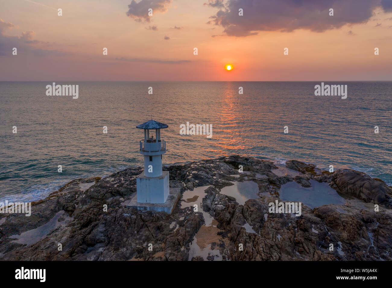 Aerial drone view of a tropical sunset behind a small lighthouse on a ...