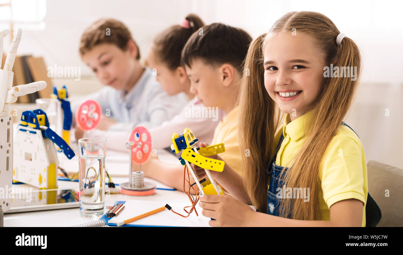 Friendly schoolgirl holding robot model in classroom Stock Photo