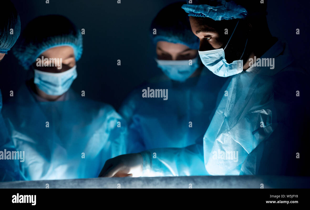 Surgeons performing surgical operation in dark operating room Stock ...