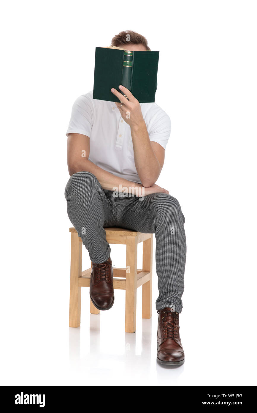 casual man sitting and reading a book covering his face with it on ...