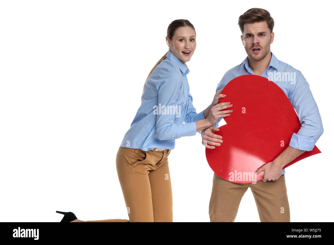 young happy couple playing with a big red heart on white background ...