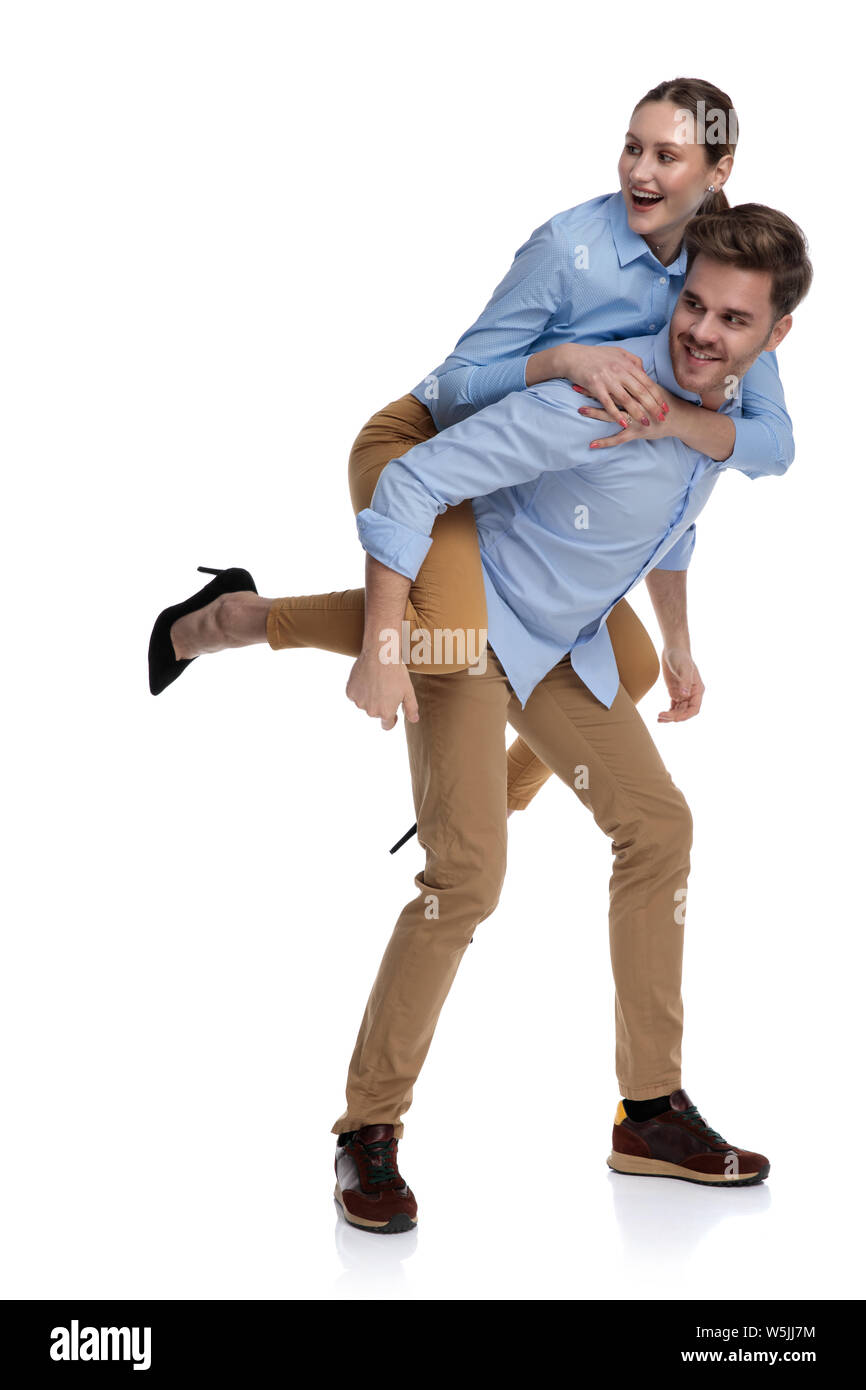 casual young man carries woman on his back and they both look to side