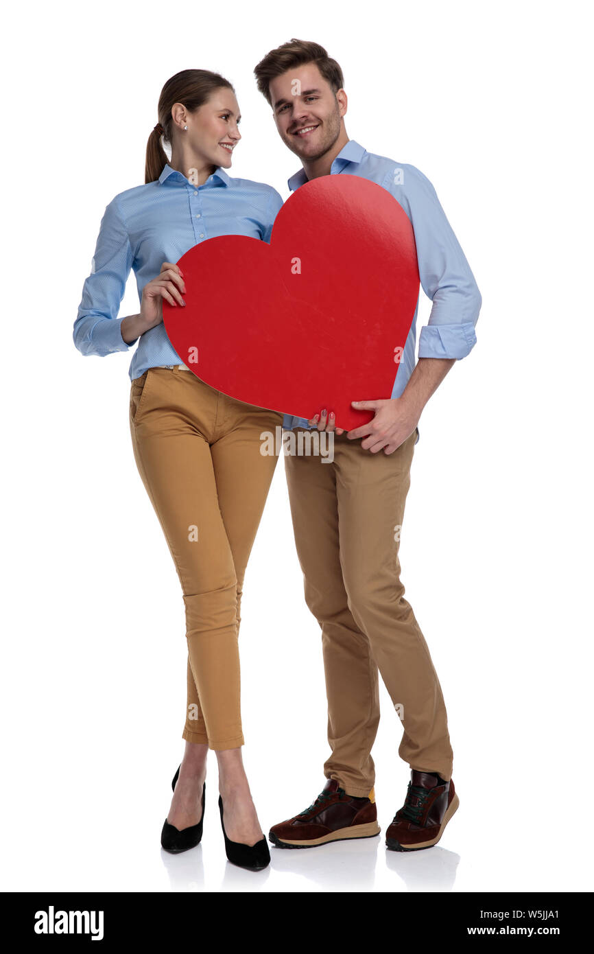 full body picture of a casual couple sharing a big heart, woman is looking at her boyfriend, on white background Stock Photo