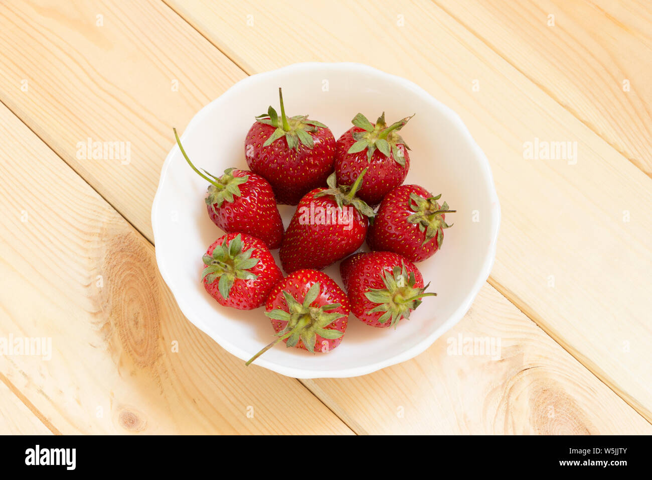 Natural delicious sweet dessert. Strawberries top view with copy space. Red mouthwatering berries in white bowl on light wooden table. Easy snack for Stock Photo