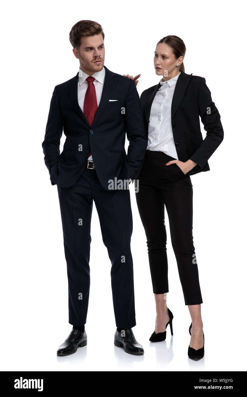 couple in business suits looking serious with hands on pockets and shoulder on white background Stock Photo